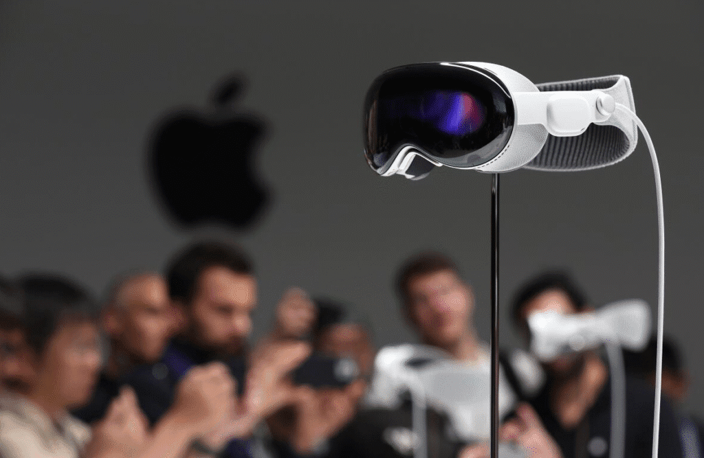 Apple Vision Pro style mixed reality headset on a stand with a blurred crowd and Apple logo in the background