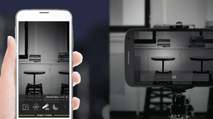 Smartphone displaying a live home security feed from an older phone used as a camera to watch a small room with stools and shelves