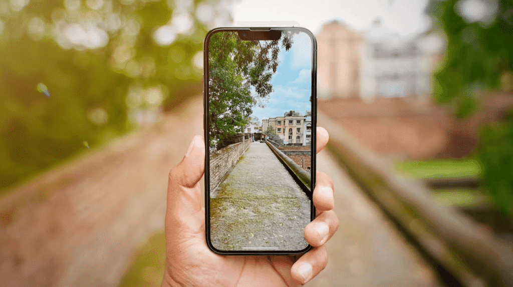 Hand holding a smartphone showing a bright outdoor walkway scene, with the real background softly blurred behind the phone screen
