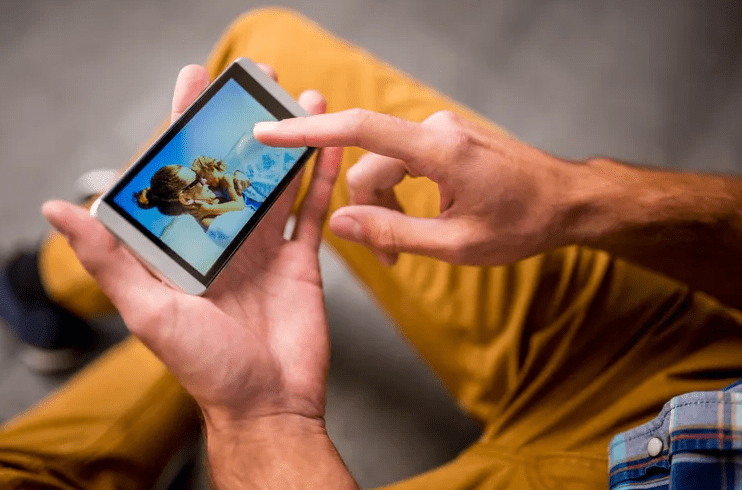 Person holding an Android phone in both hands while tapping a photo on the screen with one finger.