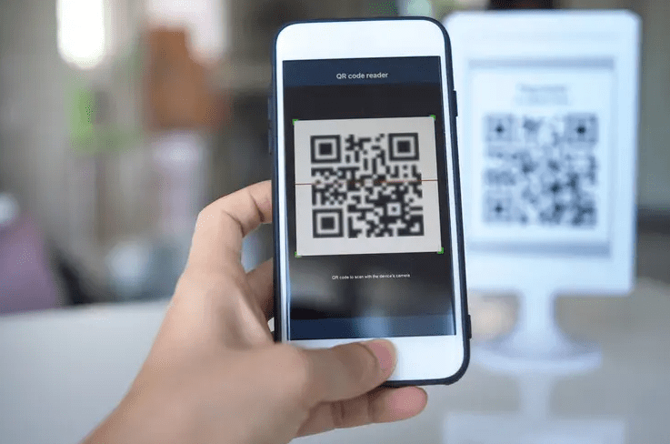 Person holding a smartphone close to the camera while using a QR code reader app to scan a code on a payment stand in the background